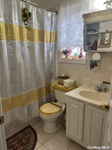 bathroom with a shower with curtain, tile patterned floors, toilet, vanity, and tile walls