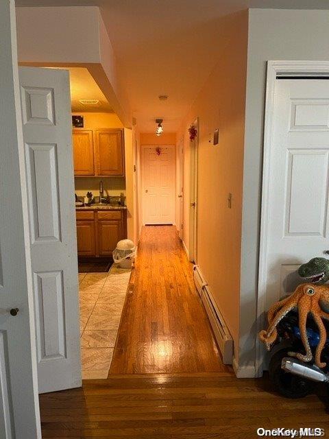 hallway with light wood-type flooring, baseboard heating, and sink