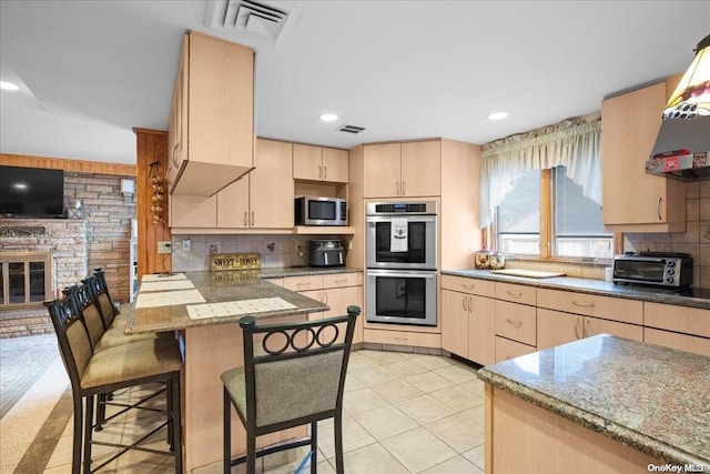 kitchen featuring stainless steel appliances, a kitchen breakfast bar, kitchen peninsula, decorative backsplash, and light brown cabinetry