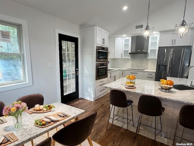 kitchen featuring white cabinets, stainless steel refrigerator with ice dispenser, vaulted ceiling, and wall chimney range hood