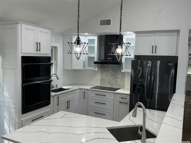 kitchen featuring wall chimney exhaust hood, hanging light fixtures, light stone counters, white cabinets, and black appliances