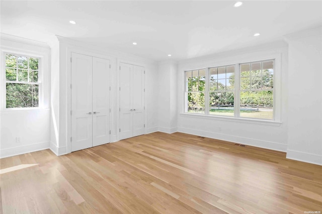 unfurnished bedroom with two closets, light hardwood / wood-style floors, crown molding, and multiple windows