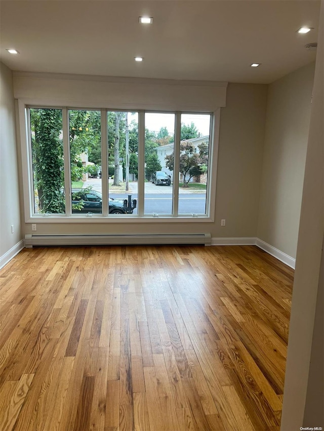 spare room with a healthy amount of sunlight, light hardwood / wood-style floors, and a baseboard radiator