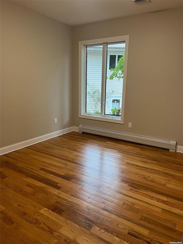 unfurnished room featuring hardwood / wood-style floors and a baseboard heating unit