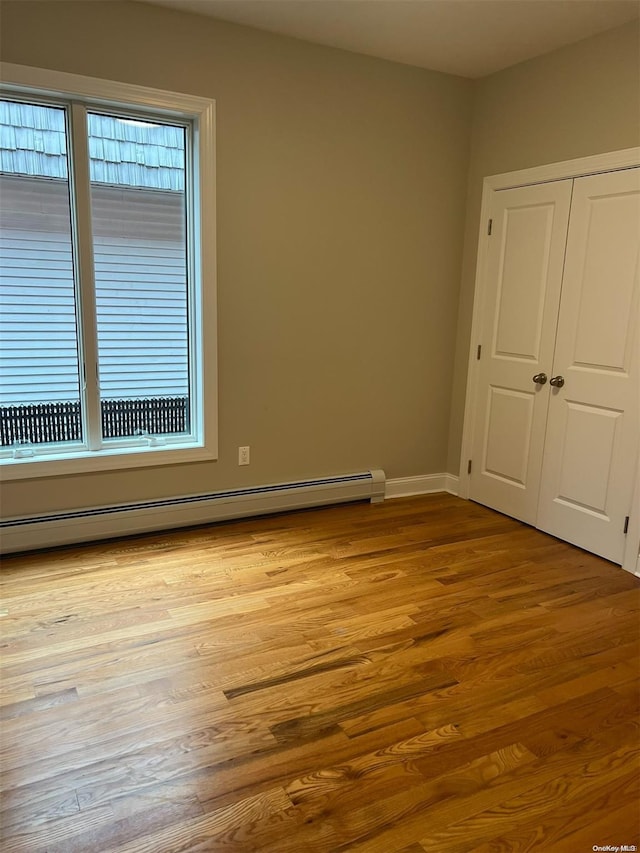 unfurnished bedroom with a closet, light wood-type flooring, and a baseboard heating unit