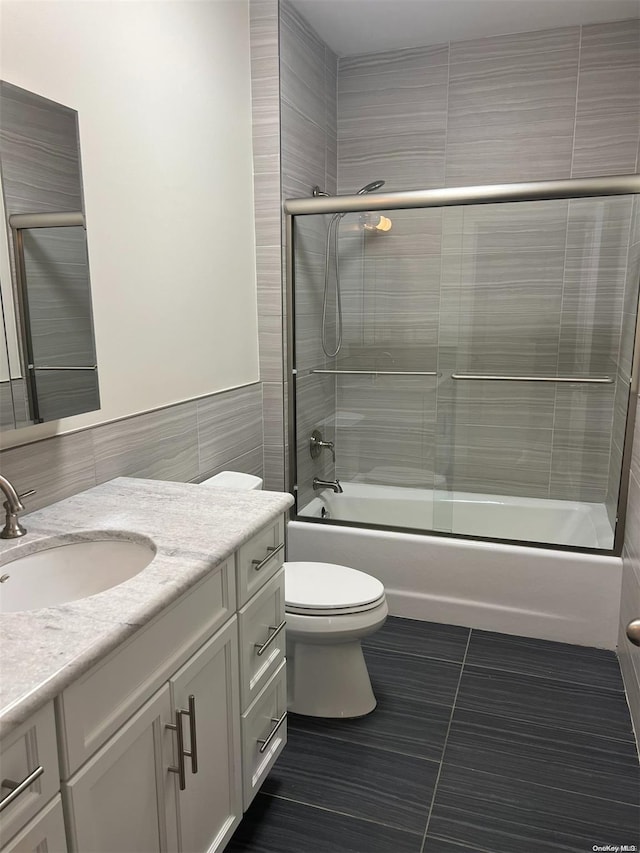 full bathroom with combined bath / shower with glass door, tile patterned floors, vanity, tile walls, and toilet