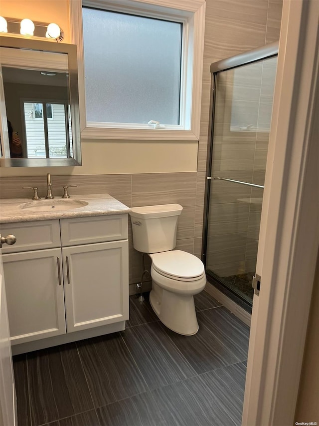 bathroom with vanity, a shower with door, tile walls, and a healthy amount of sunlight