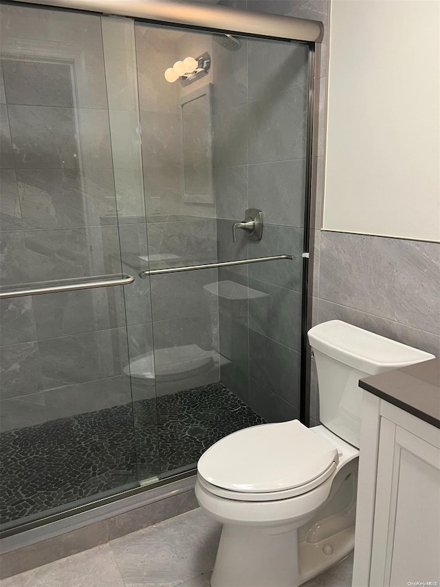 bathroom with an enclosed shower, vanity, tile walls, tile patterned flooring, and toilet