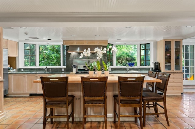 kitchen featuring wall chimney exhaust hood, light tile patterned flooring, sink, and a wealth of natural light