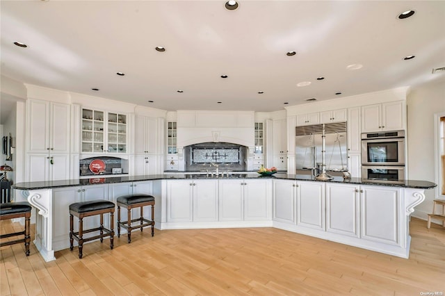 kitchen with premium range hood, sink, light hardwood / wood-style flooring, white cabinetry, and stainless steel appliances