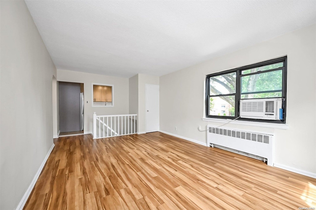 spare room featuring radiator heating unit, cooling unit, a textured ceiling, and light wood-type flooring