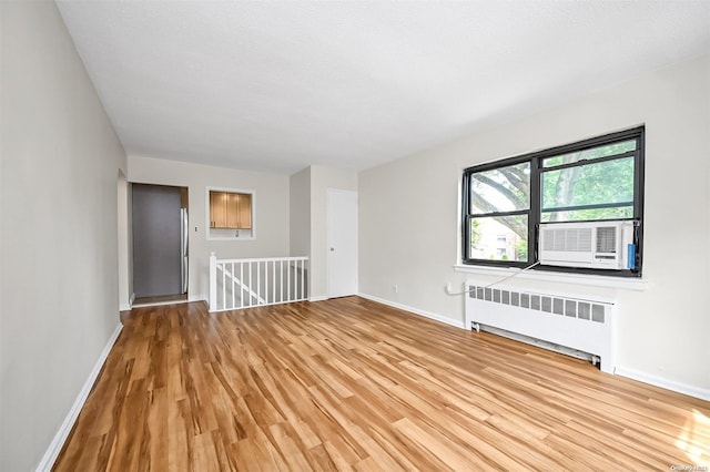 spare room featuring radiator heating unit, cooling unit, a textured ceiling, and light wood-type flooring