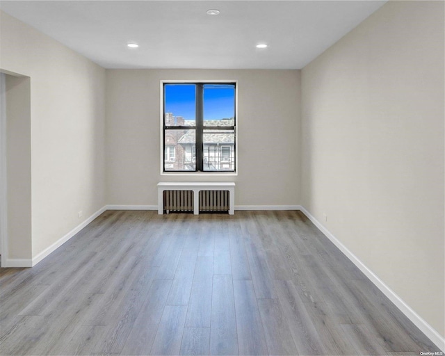 unfurnished room with radiator and light wood-type flooring