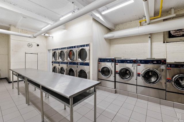 clothes washing area featuring stacked washer and dryer, light tile patterned floors, brick wall, and independent washer and dryer