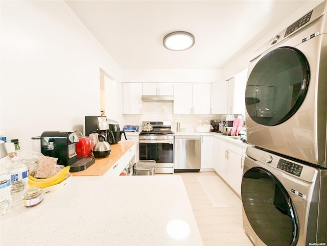 kitchen with appliances with stainless steel finishes, backsplash, stacked washing maching and dryer, and white cabinetry