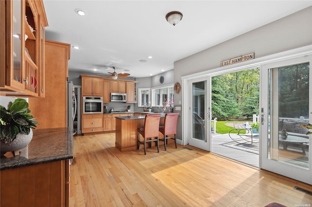 kitchen featuring ceiling fan, stainless steel appliances, light hardwood / wood-style floors, a kitchen bar, and decorative backsplash