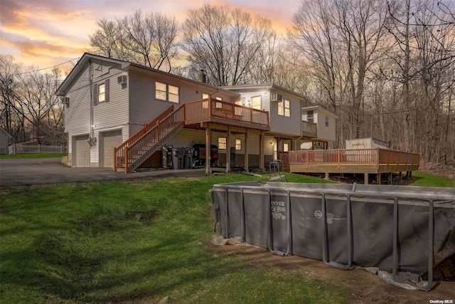 back house at dusk with a garage, a pool side deck, and a lawn