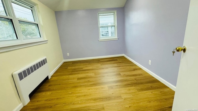 empty room featuring plenty of natural light, wood-type flooring, and radiator heating unit