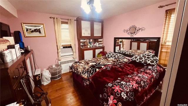 bedroom with radiator heating unit, cooling unit, and wood-type flooring