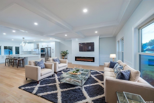 living room with light wood-type flooring, ornamental molding, a large fireplace, an inviting chandelier, and beamed ceiling