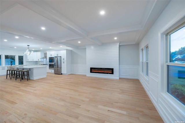 unfurnished living room featuring crown molding, a large fireplace, beamed ceiling, and light wood-type flooring