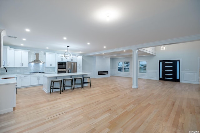 kitchen featuring a center island, light wood-type flooring, appliances with stainless steel finishes, and wall chimney range hood