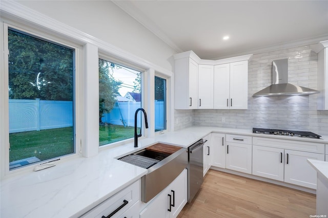 kitchen with decorative backsplash, appliances with stainless steel finishes, sink, wall chimney range hood, and white cabinetry