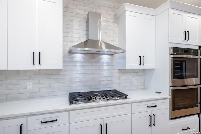 kitchen featuring appliances with stainless steel finishes, backsplash, light stone counters, wall chimney exhaust hood, and white cabinets