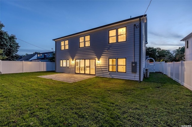 back house at dusk featuring a lawn and a patio area