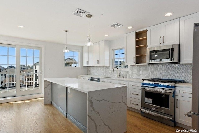 kitchen featuring light stone counters, stainless steel appliances, decorative light fixtures, white cabinets, and a center island