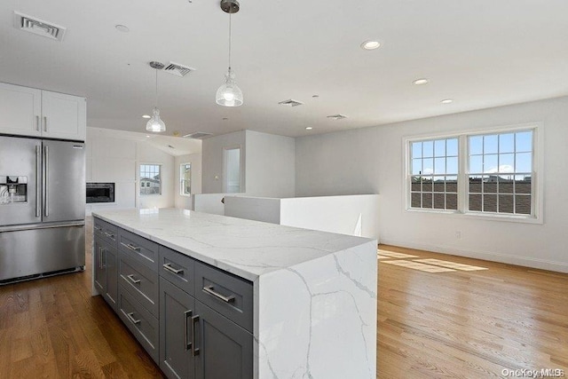 kitchen with stainless steel fridge, a healthy amount of sunlight, decorative light fixtures, a center island, and light hardwood / wood-style floors