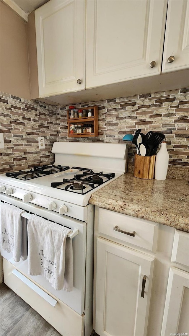 kitchen featuring backsplash, light stone counters, light hardwood / wood-style flooring, white cabinets, and white gas stove