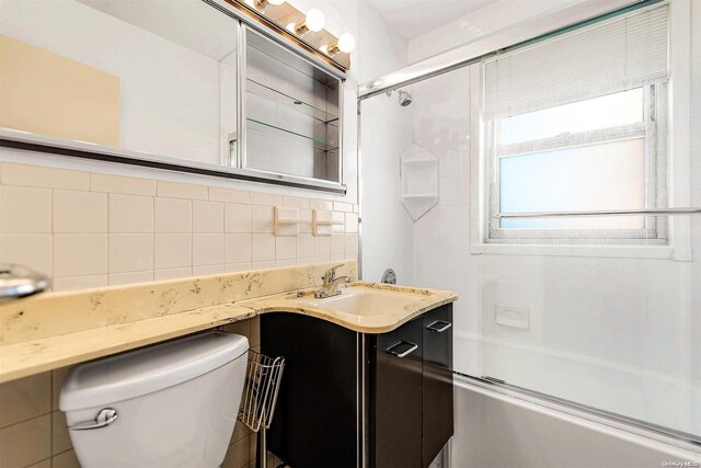 full bathroom with toilet, shower / bath combination with glass door, tile walls, vanity, and decorative backsplash