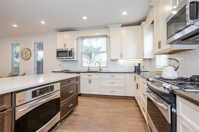 kitchen featuring appliances with stainless steel finishes, light wood-type flooring, tasteful backsplash, crown molding, and white cabinets