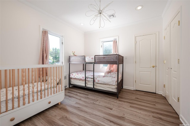 bedroom featuring light hardwood / wood-style flooring, a nursery area, crown molding, and a notable chandelier