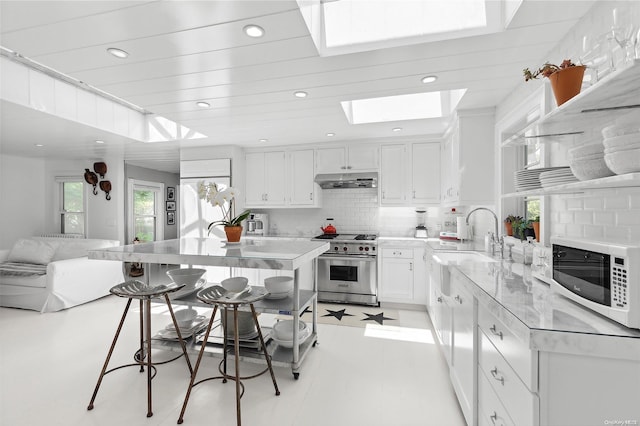 kitchen featuring backsplash, a skylight, stainless steel range, a breakfast bar, and white cabinets