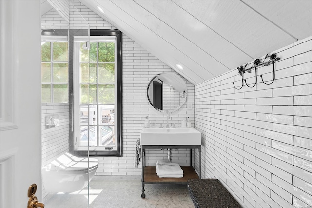 bathroom with sink, toilet, lofted ceiling, and brick wall