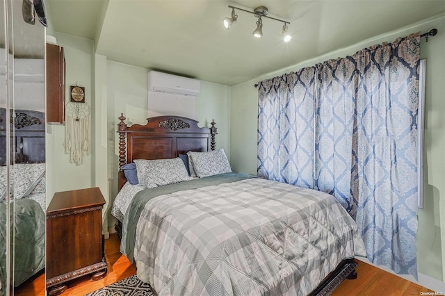 bedroom featuring a wall mounted air conditioner, rail lighting, and hardwood / wood-style flooring