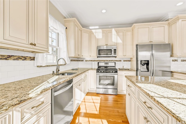 kitchen featuring cream cabinetry, stainless steel appliances, light stone counters, and sink