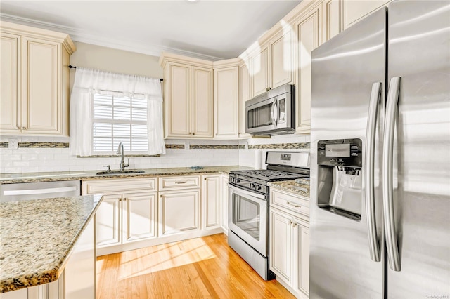 kitchen featuring light stone countertops, stainless steel appliances, sink, cream cabinets, and light hardwood / wood-style flooring