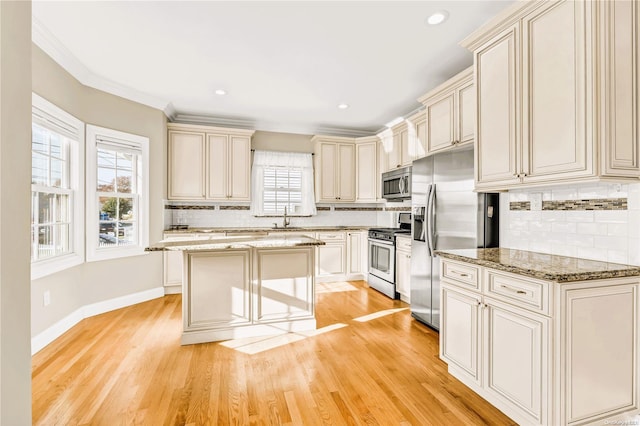 kitchen featuring stone counters, a center island, light hardwood / wood-style flooring, cream cabinetry, and appliances with stainless steel finishes