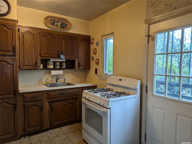 kitchen with light tile patterned flooring, sink, and white range with gas stovetop