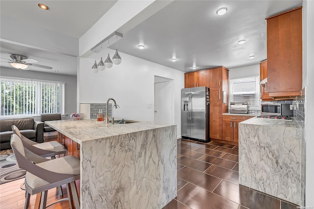 kitchen with sink, appliances with stainless steel finishes, tasteful backsplash, light stone counters, and a breakfast bar area