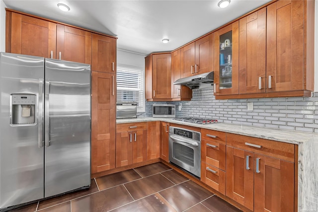 kitchen featuring dark tile patterned floors, stainless steel appliances, light stone counters, and tasteful backsplash