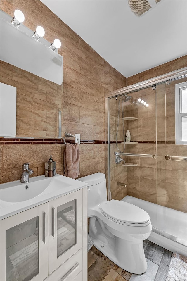 bathroom featuring hardwood / wood-style flooring, toilet, a shower with shower door, and tile walls