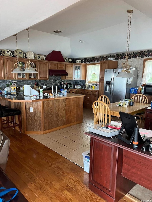 kitchen featuring stainless steel fridge with ice dispenser, hardwood / wood-style floors, hanging light fixtures, and vaulted ceiling