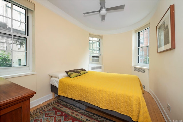 bedroom with radiator, ceiling fan, multiple windows, and hardwood / wood-style flooring