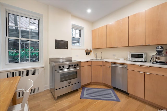 kitchen featuring radiator, sink, stainless steel appliances, light hardwood / wood-style floors, and light brown cabinetry