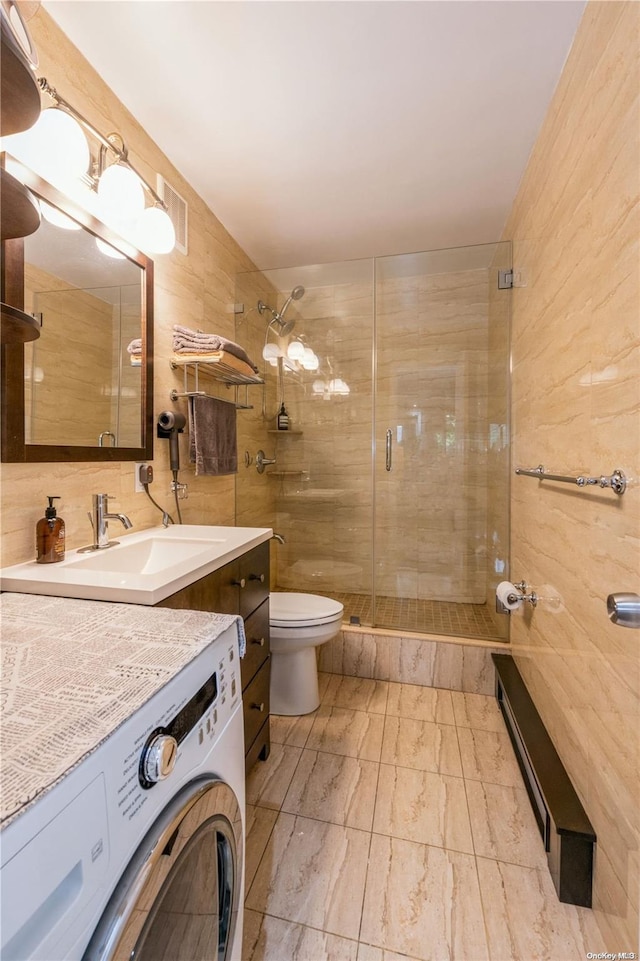 bathroom with washer / clothes dryer, toilet, vanity, a shower with shower door, and tile walls