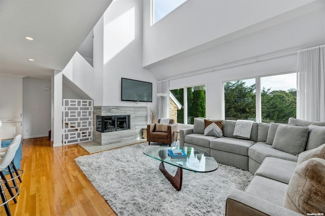 living room with a high end fireplace, wood-type flooring, a healthy amount of sunlight, and a high ceiling